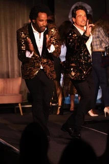Two men in black and gold patterned jackets dancing on the catwalk