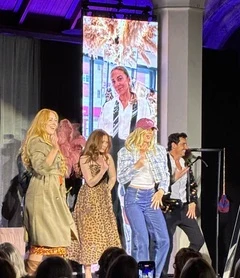 Four models on stage in front of a large video screen, with the audience in the foreground
