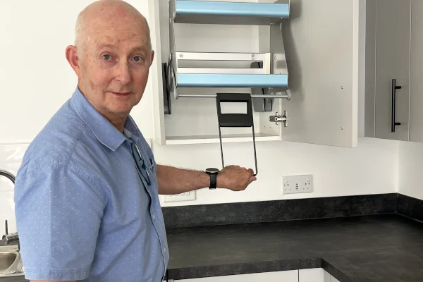 Councillor Chris Varley pulls down a drop-down shelf rack from a wall cupboard in a new Ham Close kitchen