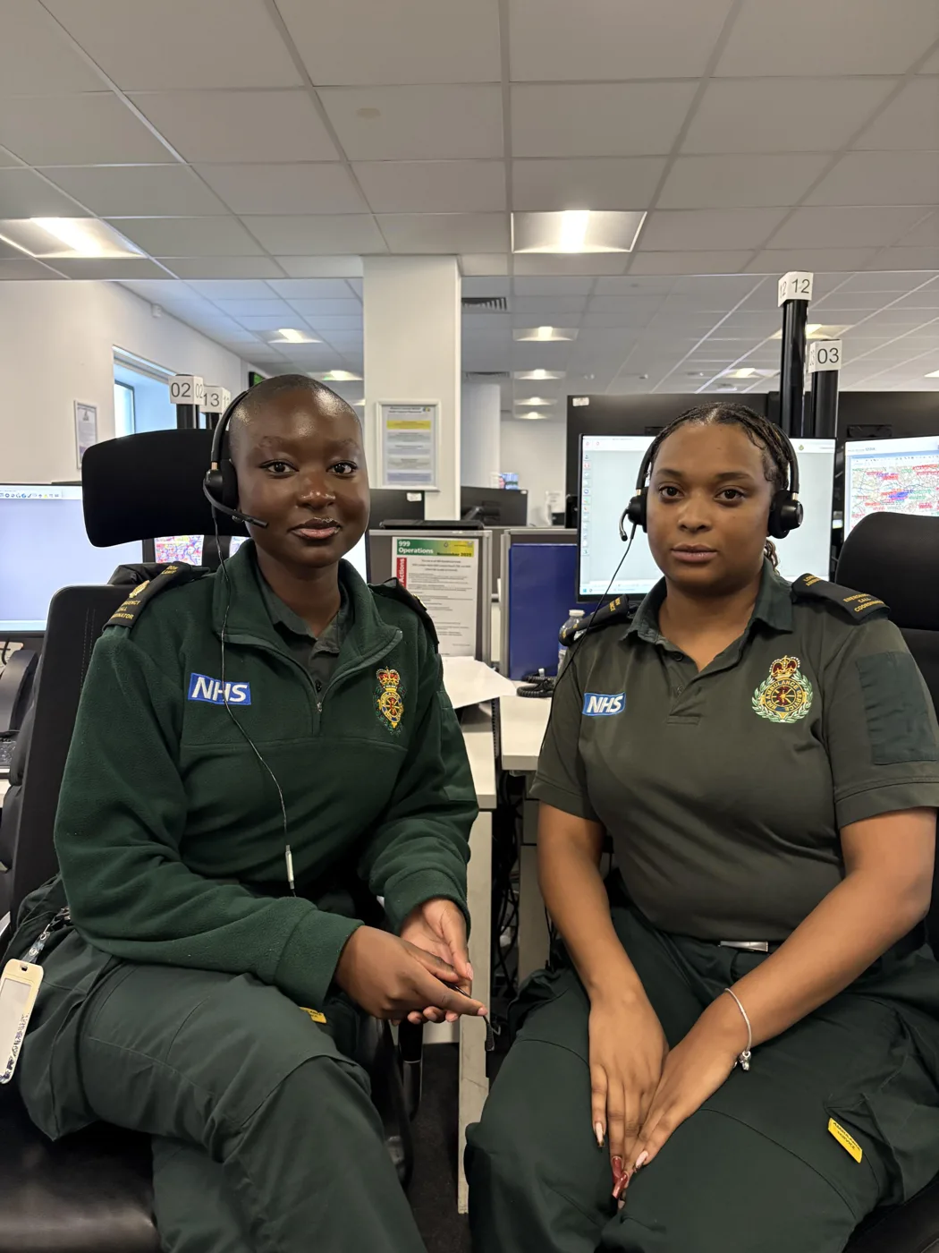 Two London Ambulance Service call handlers in green uniforms and headsets, seated side by side in a control room