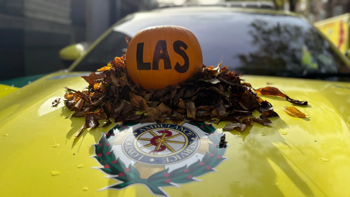 A pumpkin marked LAS on a bed of autumn leaves on the bonnet of a London Ambulance Service car