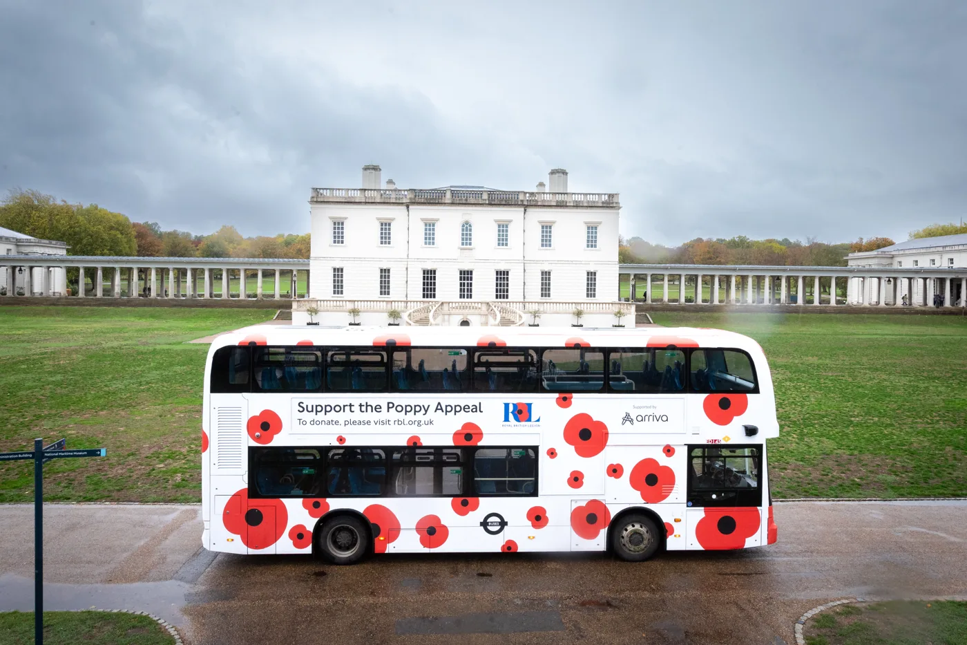 A double-decker bus wrapped in white with large red poppies and the words Support the Poppy Appeal