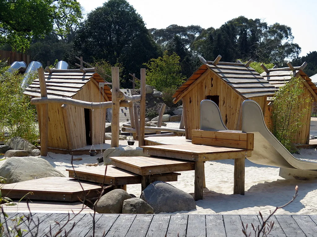 Timber play huts and a slide in the sandpit of the Children's Garden at Kew