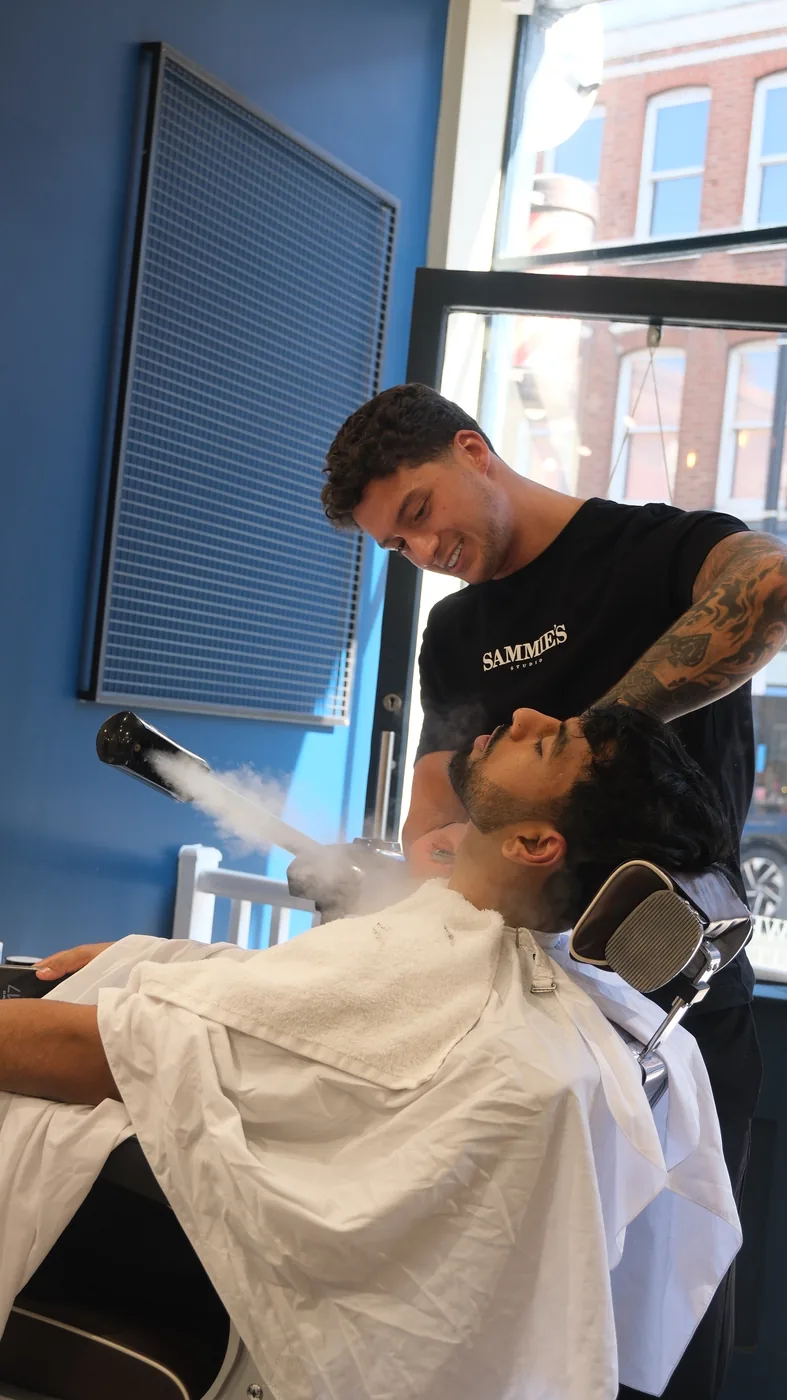 A barber applies a steam treatment to a customer reclined in a barber's chair